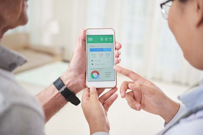 Zwei Personen halten ein Smartphone mit einer Gesundheits-App in den Händen und blicken darauf