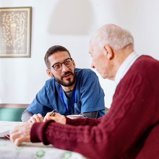 Männliche Pflegekraft unterhält sich mit einem älterem Herr.