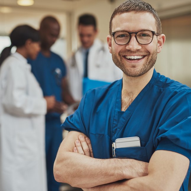 Lächelnder Arzt steht vor einer Gruppe von medizinischen Personal.