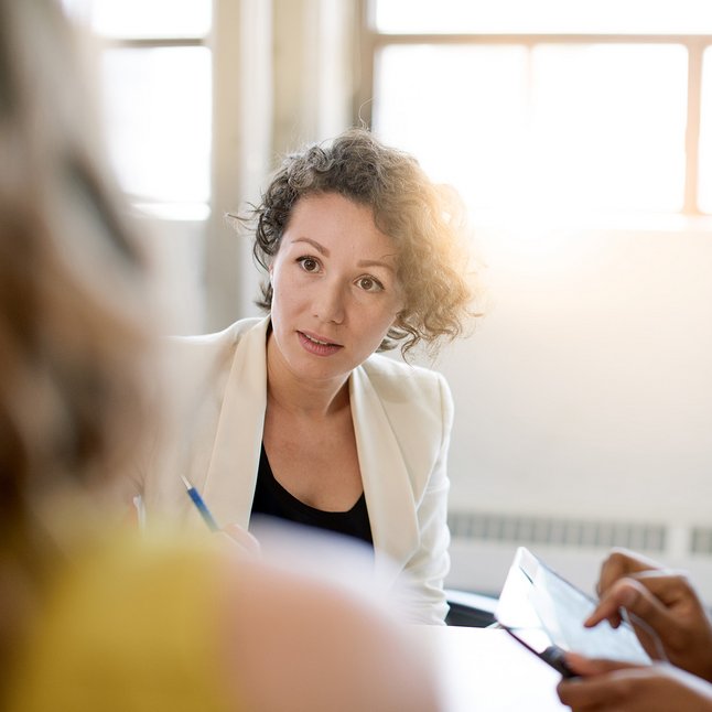 Frau im Blazer ist konzentriert im Gespräch vertieft mit anderen Personen.