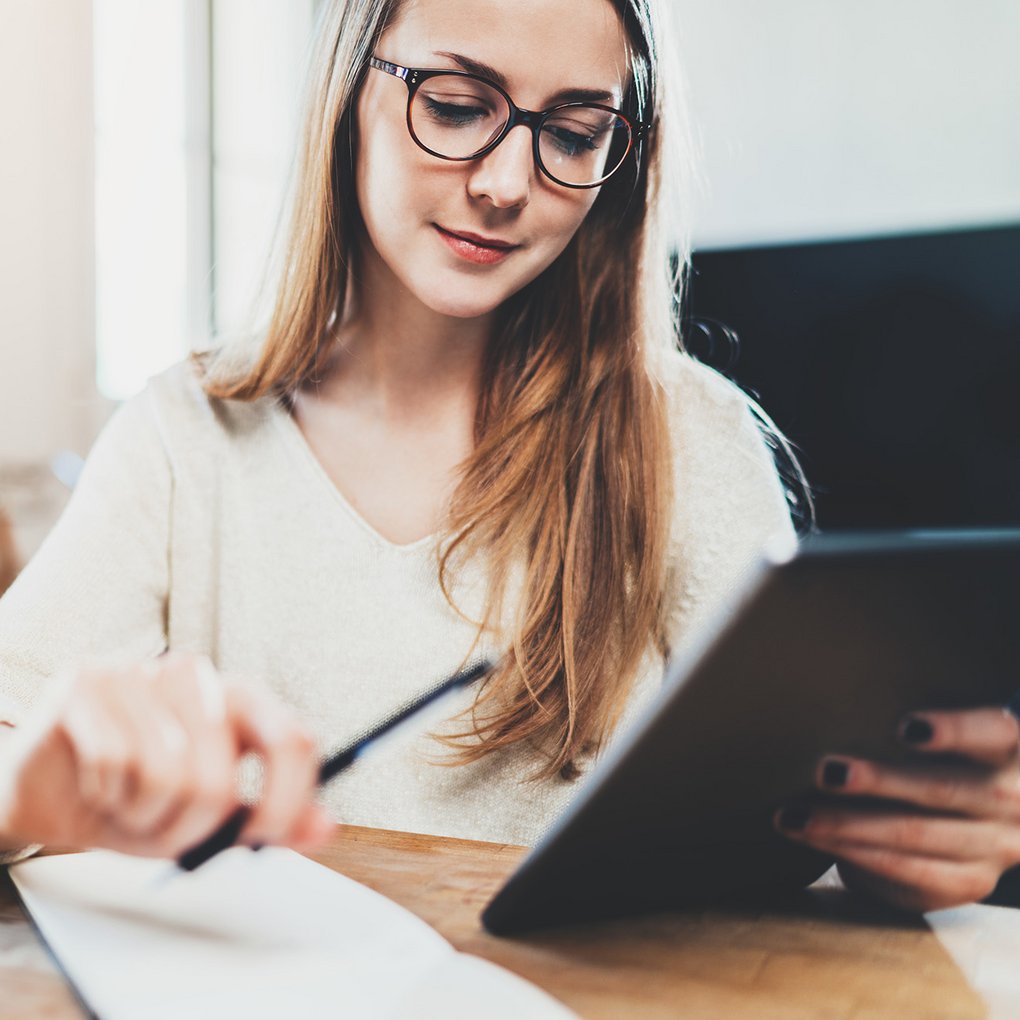 Frau mit Brille arbeitet konzentriert am Tablet.